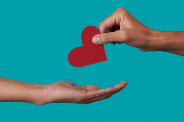 a person giving a red heart to another person on a blue background