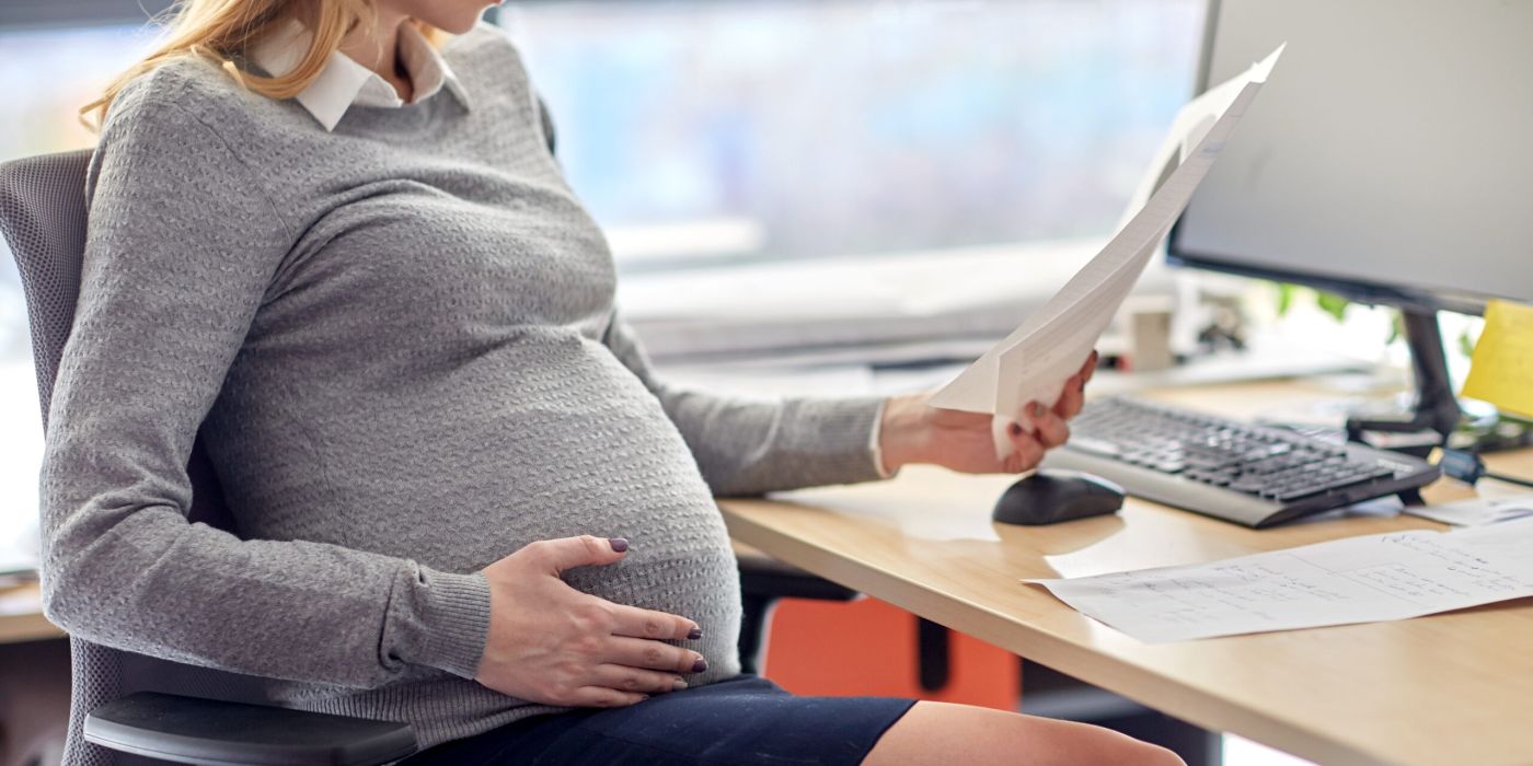 pregnancy, business and work concept - smiling pregnant businesswoman sitting at office table and reading papers