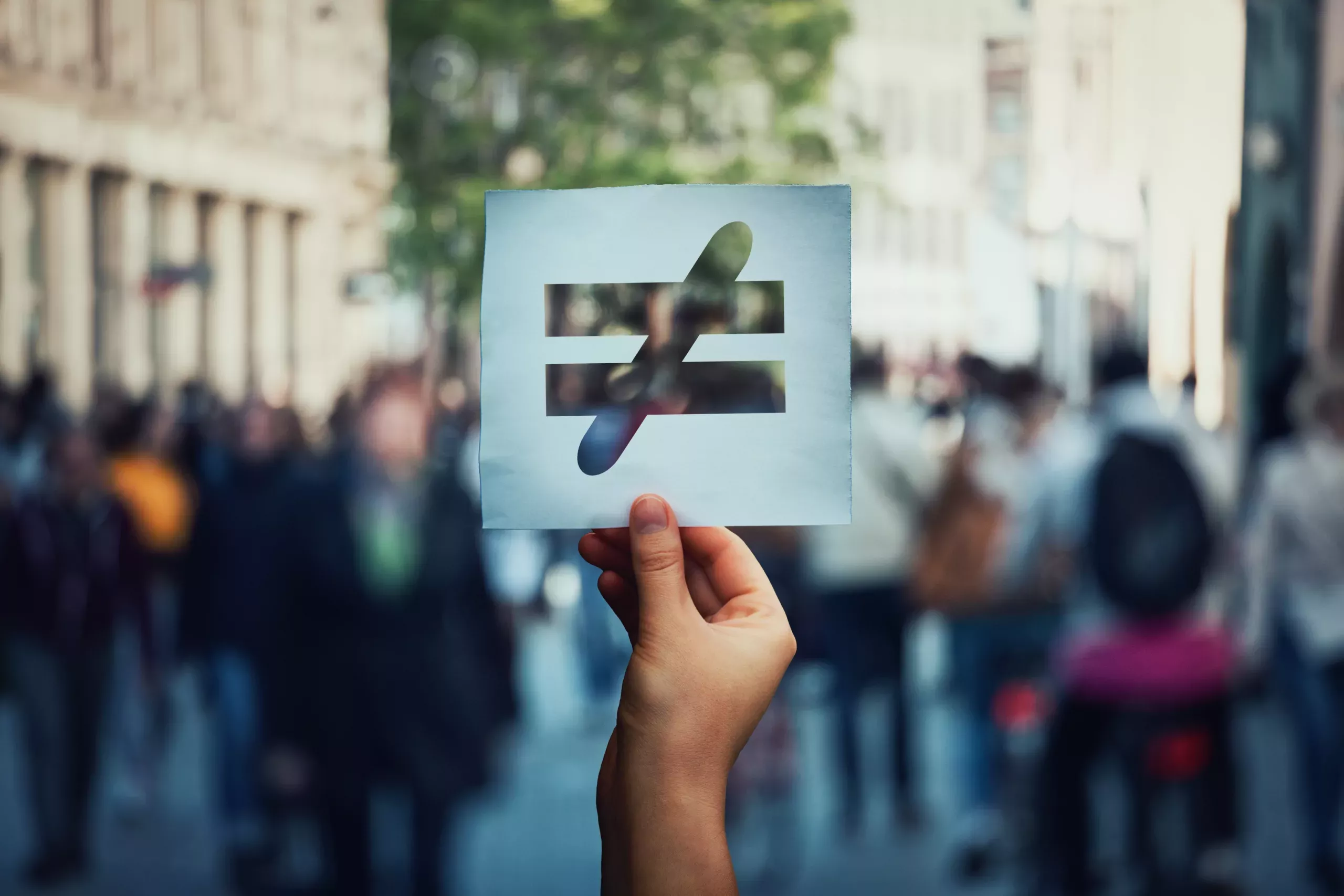 Human inequality as global social issue. Stop discrimination on grounds of race, sex or religion as hand holding a paper sheet with injustice, unfairness symbol over crowded street background.