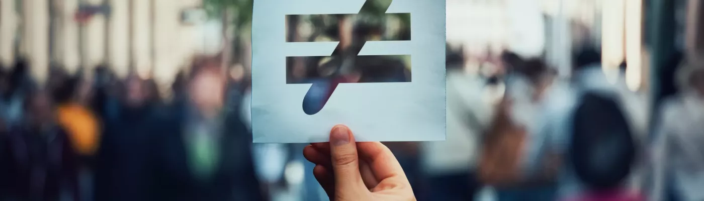 Human inequality as global social issue. Stop discrimination on grounds of race, sex or religion as hand holding a paper sheet with injustice, unfairness symbol over crowded street background.