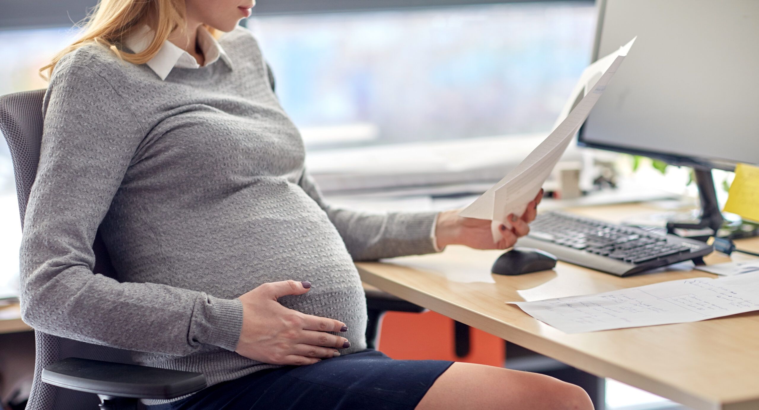 pregnancy, business and work concept - smiling pregnant businesswoman sitting at office table and reading papers