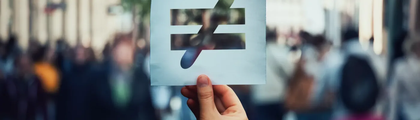 Human inequality as global social issue. Stop discrimination on grounds of race, sex or religion as hand holding a paper sheet with injustice, unfairness symbol over crowded street background.